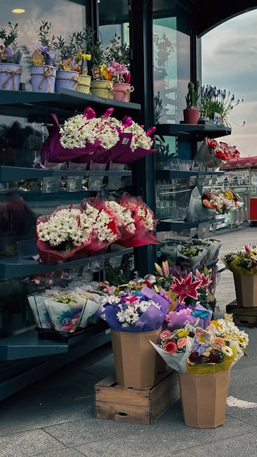 An outdoor display of fresh flower arrangements at Cowley Flowers, featuring a variety of floral bouquets including white daisies, pink lilies, and mixed seasonal blooms wrapped in colorful paper and 