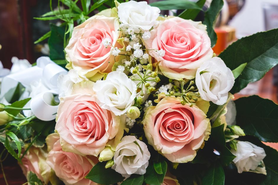 A floral arrangement featuring large, soft pink roses with gently curled petals and white lisianthus flowers with delicate, ruffled petals. The bouquet is accented with small white baby's breath and l