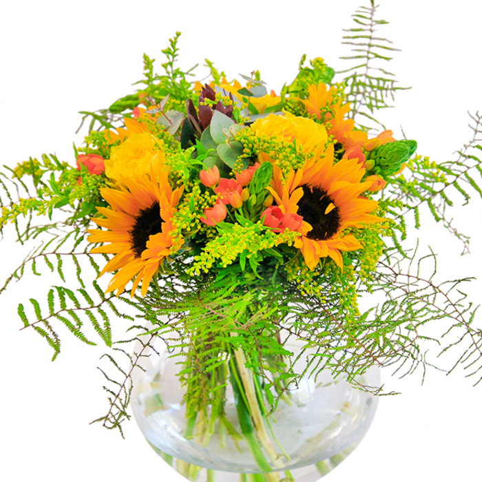 Overflowing with sunbeams and the bucolic charm of Cowley, this floral arrangement captures the exuberance of late summer. At its core, towering sunflowers blaze with deep brown centers and golden petals that exude energy and optimism. Nestled beside them, tightly furled yellow garden roses unfurl their intricate spirals, radiating classic beauty and softness. Glossy red hypericum berries are threaded throughout, their jewel tones sparkling against a backdrop of mixed greens-lush fern fronds, fine light-green fillers, and upright flower spikes, all reminiscent of the diverse foliage in Cowley's local gardens. Hints of cool blue-green eucalyptus break up the palette, providing visual relief and accentuating the rustic quality of the design. Positioned perfectly in a rounded glass vase, their stems are visible beneath the surface, contributing to the composition's clarity and architectural poise. Gentle sunlight bathes the display, highlighting the vivid colors and creating a welcoming, uplifting mood. The blend of delicate rose scent and crisp, fresh greenery lingers in the air, making this arrangement a fitting centerpiece for celebrations-birthdays, housewarmings, or simply to bring a ray of Cowley sunshine indoors. Lovingly arranged, it speaks to the neighborhood's spirit of community, artistry, and the enduring joy found in flowers.