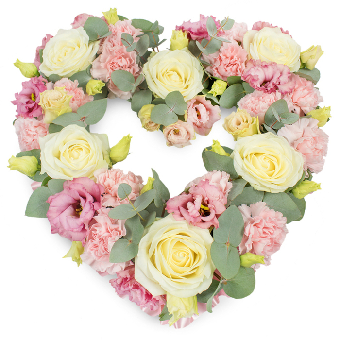 A graceful heart-shaped floral tribute fills the frame, its pastel blooms carefully composed against a pristine white background, reminiscent of arrangements prepared for intimate services around Cowley. The heart is completely filled, giving the impression of a soft, abundant cushion of flowers shaped into a symbol of love. Cream and pale yellow roses take pride of place, their velvety petals arranged in tight spirals that open gently toward the edges, each bloom conveying calm, enduring affection. Tucked closely around them are generous clusters of pale pink carnations, their frilled petals layered in soft waves, creating a delicate, almost cloud-like texture. Scattered throughout the design are deeper pink and mauve lisianthus flowers, their more open, trumpet-shaped blooms lending a romantic richness that draws the eye, adding depth and subtle shadows among the lighter tones. Cool, silvery-green eucalyptus leaves thread gracefully between the flowers, their rounded forms and muted colour adding both structure and a restful visual balance. Small, yellow-green buds emerge from the foliage and between petals, suggesting freshness and newly cut stems, as if the wreath has just been finished for same-day delivery to a Cowley chapel or funeral home. The overall composition is dense yet harmonious, with each flower placed to maintain the clean heart outline while creating a sense of fullness and gentle luxury. This tribute is especially suited to funerals, memorial gatherings, or heartfelt anniversary remembrances, offering a compassionate way to express sympathy, gratitude, and enduring love. The white backdrop ensures that every shade of cream, blush pink, and eucalyptus green remains clear and luminous, turning the wreath into a quiet focal point of beauty and solace.